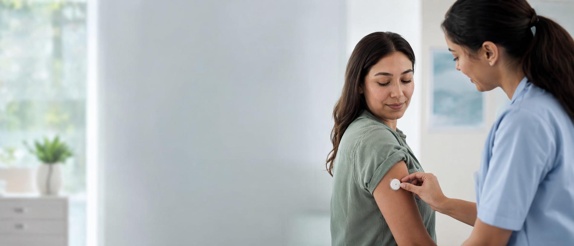 A nurse applying a continuous glucose monitor sensor to a patient's upper arm in a bright clinic